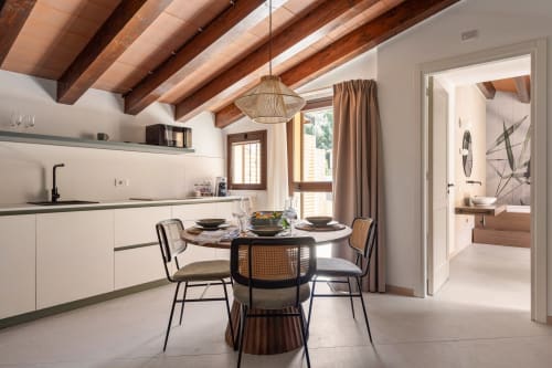 Modern kitchen-dining area at Dimora Silva Nature Suites with exposed wood beams, round table, and rattan chairs