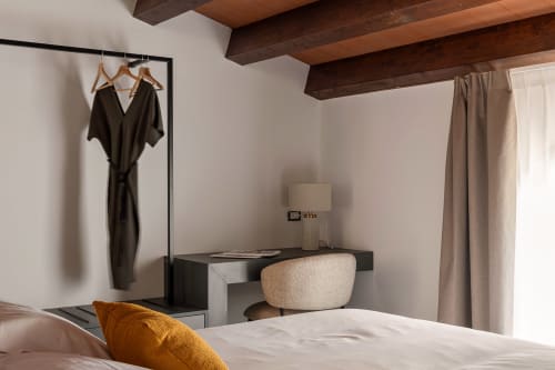 Modern bedroom at Dimora Silva Nature Suites with exposed wooden beams, black desk, beige chair, and hanging black robe on