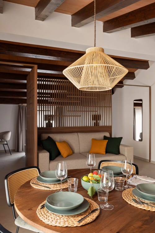 Dimora Silva Nature Suites dining area with wooden beams, woven pendant light, and beige sofa with forest green and gold