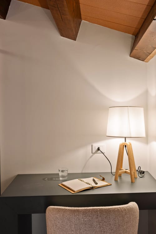 Spazio di lavoro moderno presso Dimora Silva Nature Suites con lampada in legno, quaderno e bicchiere d'acqua su scrivania scura