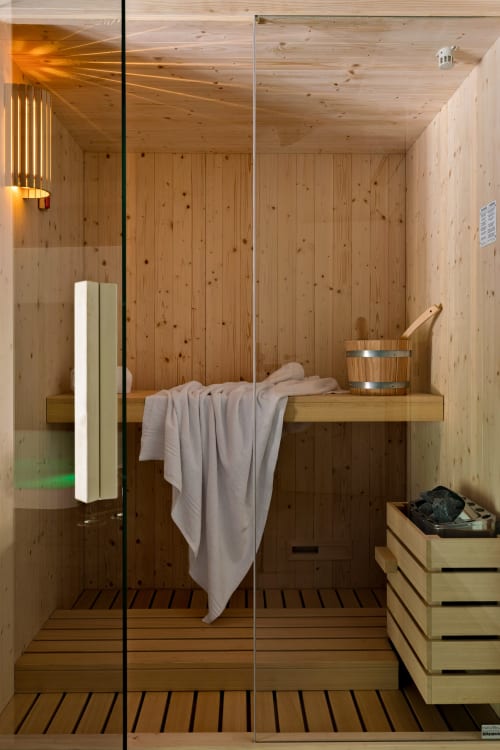 Interno moderno della sauna presso Dimora Silva Nature Suites con panche in legno, asciugamani e porta in vetro a San Martino delle Scale