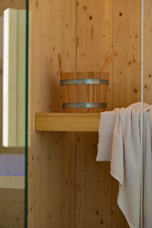 Interno in legno della sauna presso Dimora Silva Nature Suites con secchio in cedro, mestolo e asciugamano su ripiano