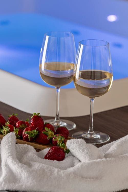 Due calici di vino bianco con fragole fresche affacciate sulla piscina azzurra di Dimora Silva Nature Suites