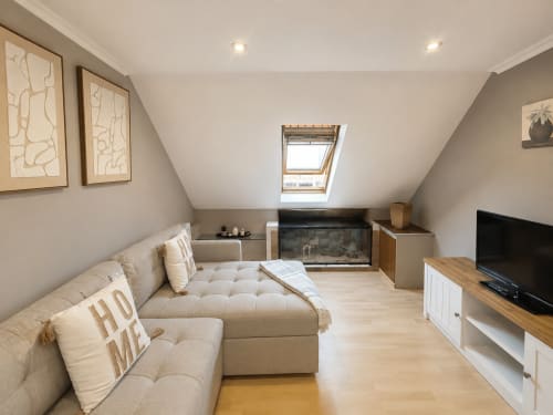 Acogedor dormitorio en el ático de Holibai en Baiona con sofá crema, tragaluz, chimenea y zona de entretenimiento con TV