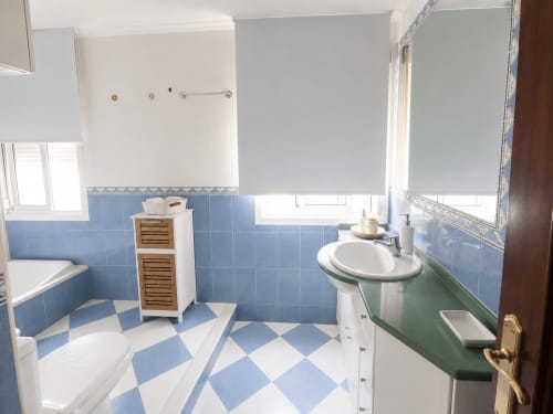 Baño con azulejos azules y blancos del hotel Holibai en Baiona, con lavamanos pedestal e inodoro