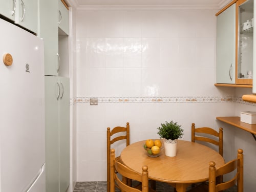 Área de comedor en la cocina del hotel Holibai en Baiona con mesa de madera, sillas y moderno azulejo blanco