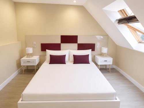 Moderno dormitorio abuhardillado en el hotel Holibai de Baiona con cama queen, detalles burdeos, claraboya y mesitas blancas