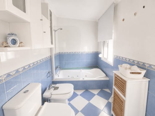 Baño moderno en Holibai Baiona con azulejos azules y blancos, bañera, inodoro, lavabo y mueble de almacenamiento de madera