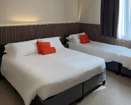 Camera d'hotel moderna con due letti, biancheria bianca, cuscini rossi, testiera in legno scuro e vista sul giardino presso Maison ì Room a Reggio