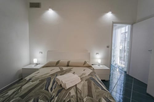 Camera moderna dell'Antico Palazzo del Corso con letto matrimoniale, biancheria neutra, comodini con lampade e accesso al balcone