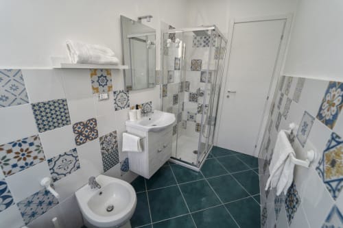 Bagno luminoso con piastrelle blu e bianche decorate, lavabo, wc e doccia all'Antico Palazzo del Corso