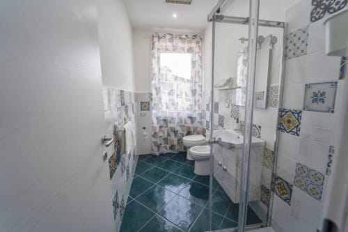 Bagno moderno in Antico Palazzo del Corso con pavimento in piastrelle turchesi, rivestimenti decorativi, box doccia e doppio lavabo.