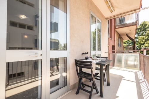 Balcone soleggiato con tavolo e sedie neri presso l'appartamento AmazHome a Rimini, vista sulla città