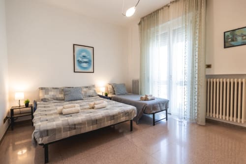 Ampia camera da letto con letti matrimoniali, balcone, vista sulla città e arredamento moderno presso l'hotel AmazHome a Rimini