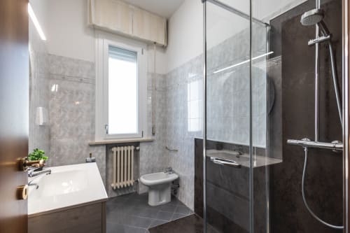 Bagno moderno nell'appartamento AmazHome di Rimini con lavabo bianco, wc, box doccia in vetro e piastrelle scure