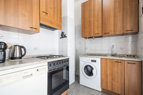 Cucina moderna con mobili in legno, fornello a gas, lavatrice e top in granito nell'appartamento AmazHome a Rimini