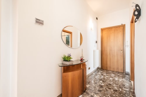 Ingresso moderno dell'appartamento AmazHome a Rimini con porte in legno, specchio rotondo e consolle con pianta