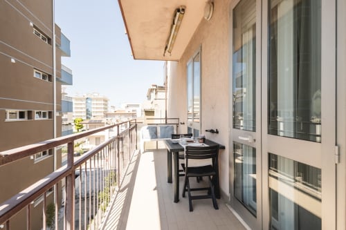 Balcone soleggiato di appartamento a Rimini con tavolo da pranzo, vista sulla città e arredamento moderno presso AmazHome