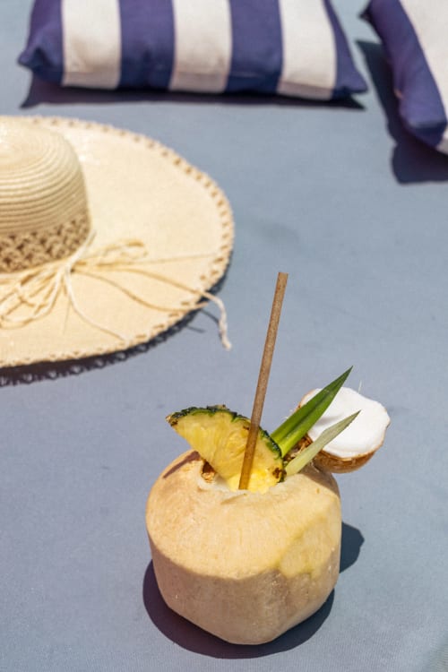 Cóctel tropical en coco en Hotel Isla Mujeres Centro con sombrero de paja y cojín a rayas