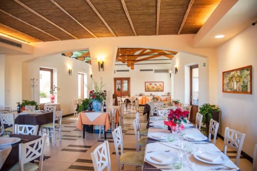 Elegante sala da pranzo dell'Hotel Ristorante alle Querce a Castelbuono con sedie bianche, travi in legno e tavoli decorati