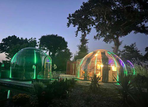 Les chambres en dôme géodésique illuminées de l'hôtel Bubble Jade la nuit à Bazouges-la-Pérouse avec vue sur le jardin et éclairage néon