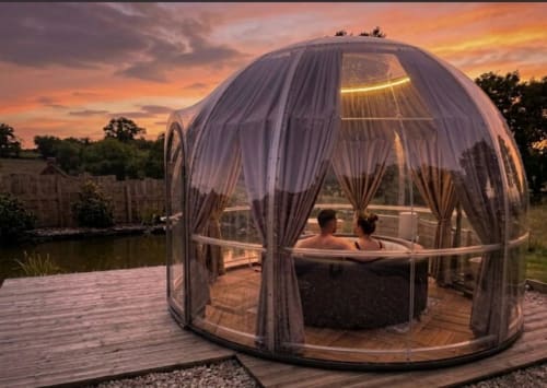 Couple se relaxant dans un jacuzzi privé au cœur d'un dôme géodésique de l'hôtel Bubble Jade, Bazouges la Pérouse, au coucher de soleil avec vue sur le jardin