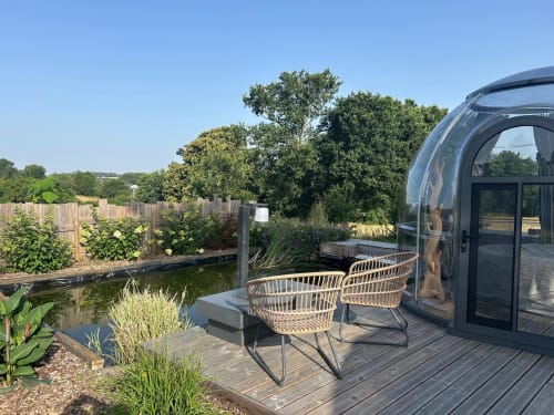 Chambre d'hôtel Bubble Jade avec chaises tressées sur terrasse en bois donnant sur un étang et jardins à Bazouges la Pérouse, France