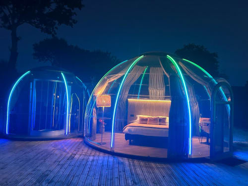 Dôme transparent illuminé de la chambre de l'hôtel Bubble Jade la nuit, avec éclairages néon vert et bleu, lit intérieur visible