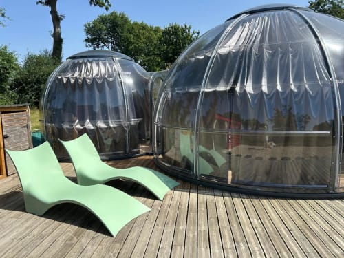 Deux dômes bulles transparents avec chaises longues vertes sur terrasse en bois à l'hôtel Bubble Jade, vue sur le jardin
