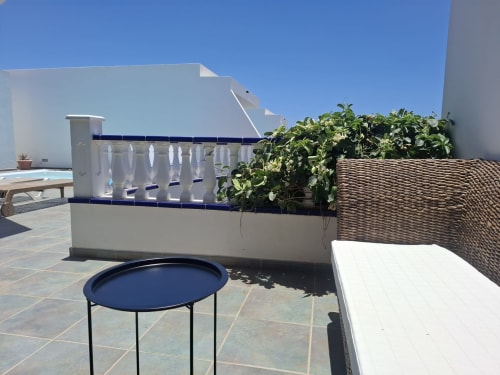 Terraza con vistas en Villas del Mar: mesita azul, tumbona blanca, cerco tejido y plantas exuberantes en Puerto Calero