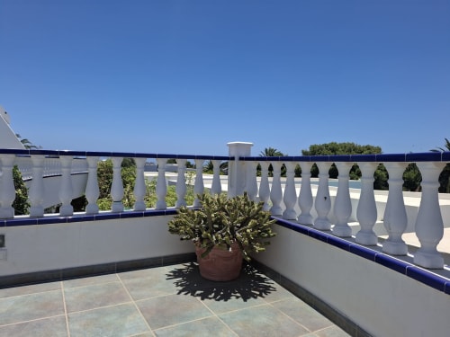 Soleada terraza con balaustrada blanca, cactus en maceta y cielo azul despejado en Villa 6, Puerto Calero
