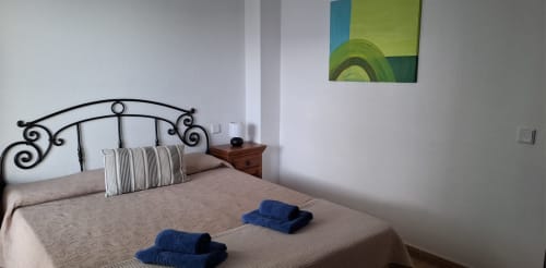 Dormitorio en Villas del Mar con cama de hierro forjado ornamentado, toallas azules, almohadas a rayas y mesita de noche de madera