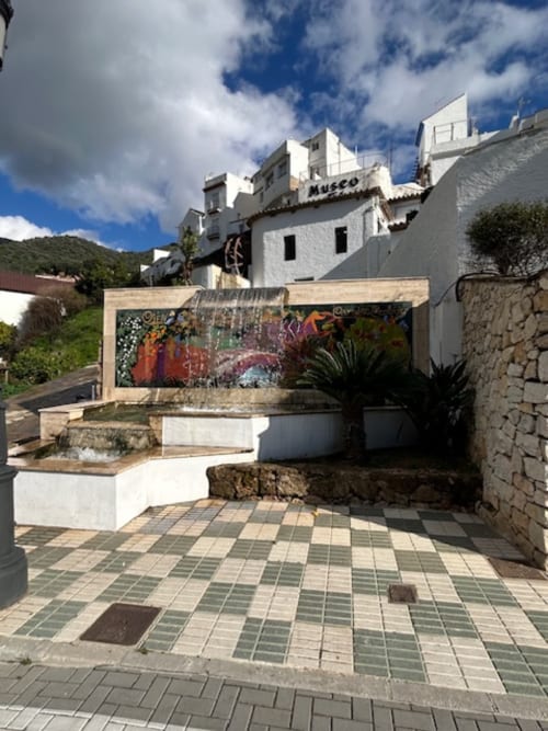 Patio de la casa rural Marbella Views B&B en Ojén con mural colorido, fuente de agua y edificio blanco estilo museo