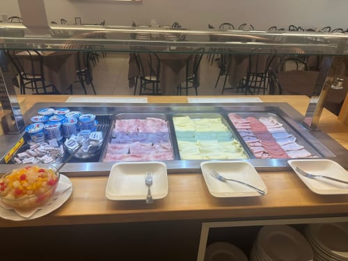 Breakfast buffet display at VERDI hotel in Jesolo featuring cold cuts, cheese, yogurt, and fresh fruit salad