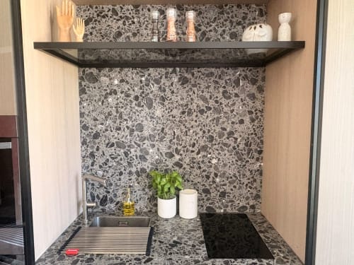 Modern kitchenette in Le Havre apartment with terrazzo backsplash, black shelf, potted plant, and stainless steel sink.