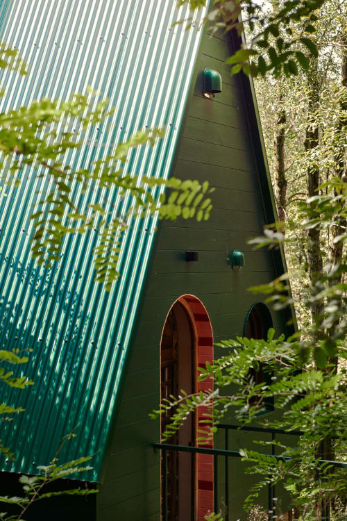 Entrée de Micro Palaces Vaulx BnB avec porte cintrée rouge, murs verts et verdure luxuriante autour de l'architecture moderne