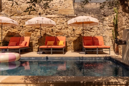 Luxury pool area at Le Prieuré Notre-Dame, Montfrin with orange loungers, umbrellas and stone wall