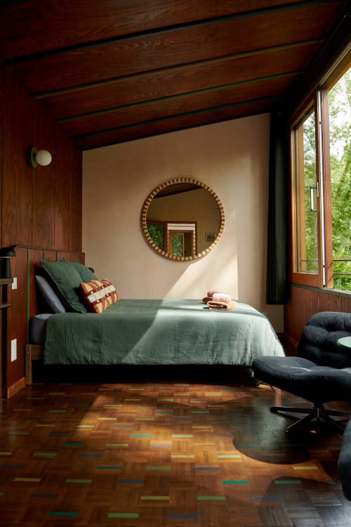 Chambre moderne aux Micro Palaces Vaulx avec poutres en bois, linge vert, miroir rond et parquet coloré