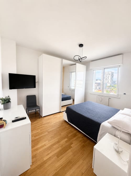 Camera moderna in Bicocca Flat B Milano con letto queen, armadio bianco, TV, parquet e vista sulla città