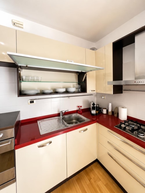 Cucina moderna con armadietti crema, piano rosso, elettrodomestici in acciaio e mensole in vetro, Bicocca Milano