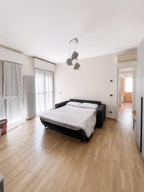 Camera moderna con divano letto nero, pavimenti in legno e illuminazione a sospensione presso Bicocca Flat Milano