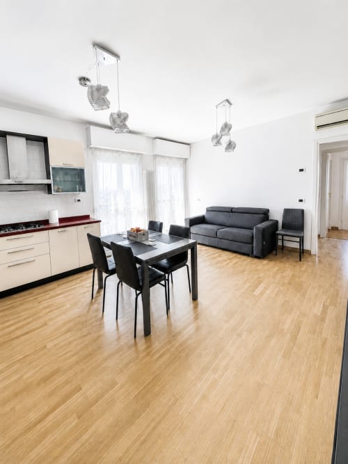 Luminoso open-plan a Bicocca Flat Milano con cucina, tavolo da pranzo, divano grigio e pavimenti in legno