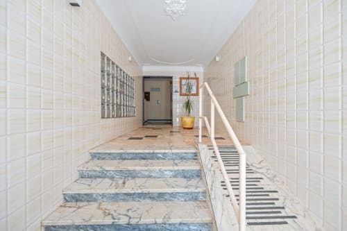 Entrada do edifício Happy Nest AL com escadaria em mármore e paredes em azulejo branco em Armação de Pêra
