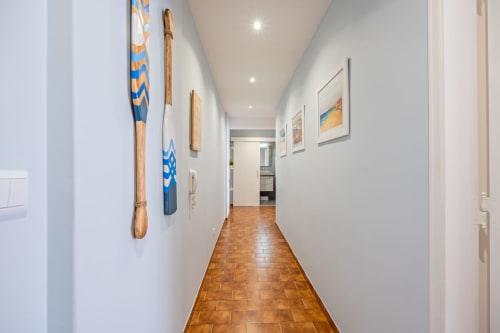 Corredor moderno da Happy Nest AL em Armação de Pêra com remos decorativos e obras de arte emolduradas em paredes brancas