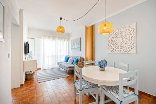 Apartamento Pêra Breeze no Happy Nest AL com mesa de jantar, sofá com almofadas azuis, luminárias amarelas e vista da cidade