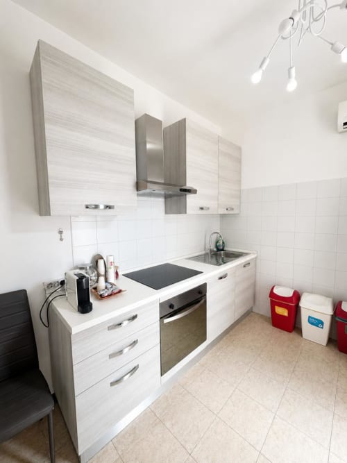 Cucina moderna nel Bicocca Flat Milano con mobili bianchi, elettrodomestici in acciaio inox e rivestimento in piastrelle