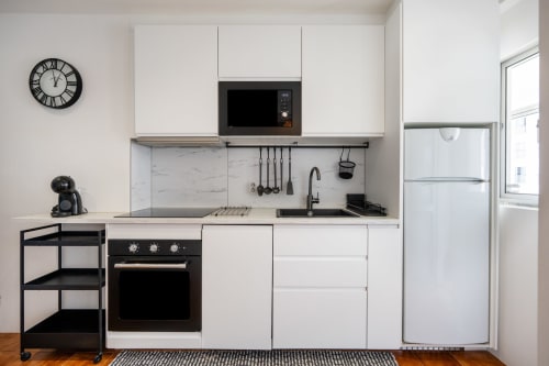 Cozinha moderna branca com eletrodomésticos pretos e painel de mármore no apartamento Pêra Breeze, Armação de Pêra