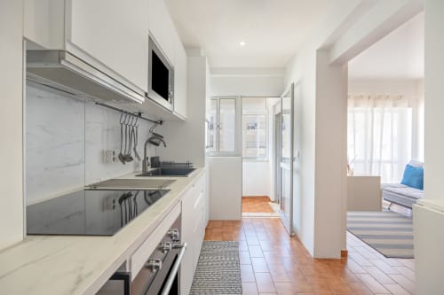 Cozinha moderna estilo galera com armários brancos, painel de mármore e eletrodomésticos em aço inoxidável no apartamento Pêra Breeze do Happy