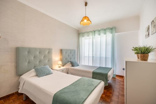 Quarto duplo luminoso no Happy Nest AL com cabeceiras capitonadas, detalhes em verde e acesso à varanda em Armação de Pêra