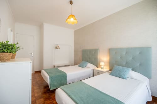 Quarto duplo com cabeceiras azul-petróleo e roupa de cama branca no hotel Happy Nest AL em Armação de Pêra, Portugal